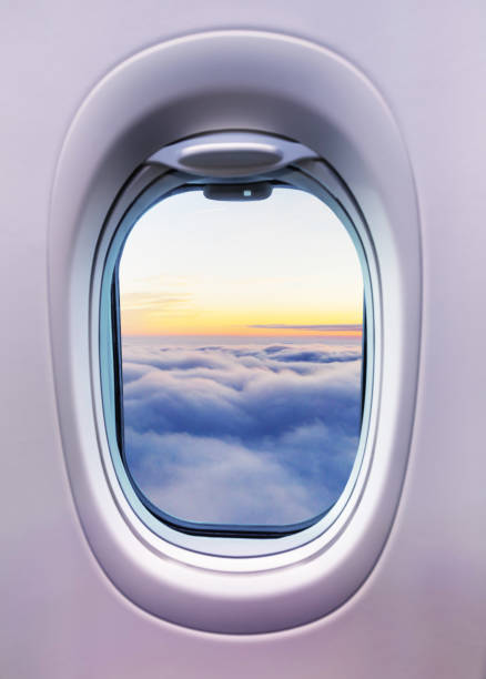 Airplane interior with window view of sunset above clouds.