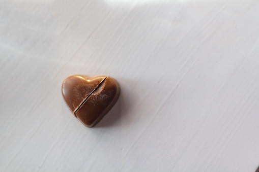 Chocolate heart candy cut in half on white wooden table with copy space