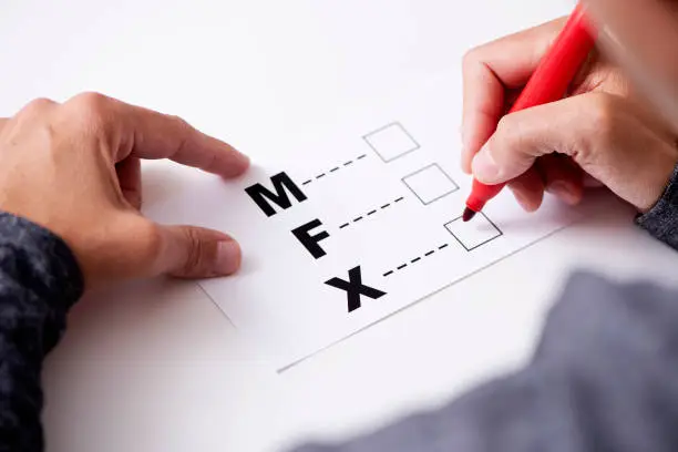 closeup of a young caucasian person about to mark on the X in a form with the letters M for male, F for female and X for the third gender category
