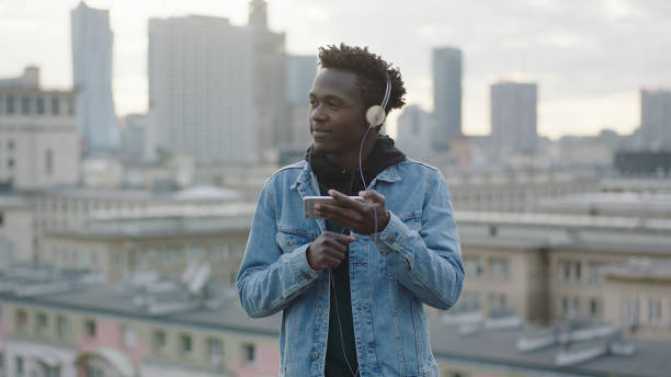 istock Young man listening music from smart phone. Rooftop view 1129370435