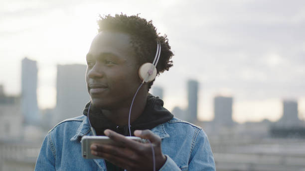 istock Young man listening music from smart phone. Rooftop view 1129370472