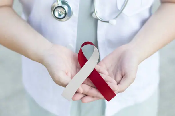 Red and white ribbon awareness in doctorâs hand for Aplastic Anemia,Deep Vein Thrombosis (DVT),Head & Neck Cancer,Oral Cancer,Squamous Cell Carcinoma.