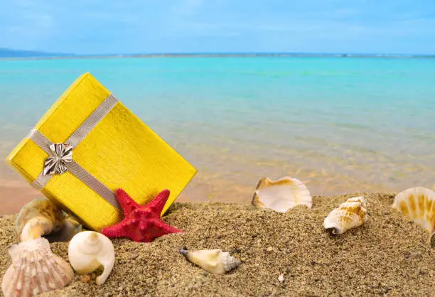 Photo of Gold gift box on sand with summer sea background