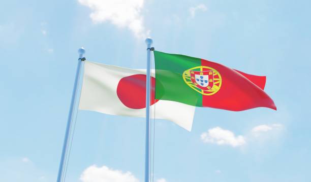 istock Portugal and Japan, two flags waving against blue sky 1129374571