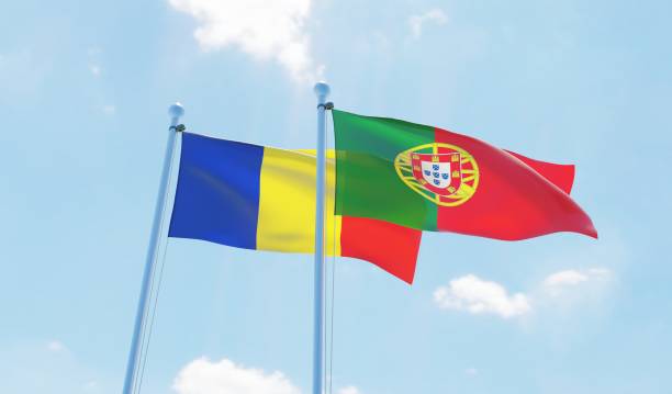 istock Portugal and Romania, two flags waving against blue sky 1129374674