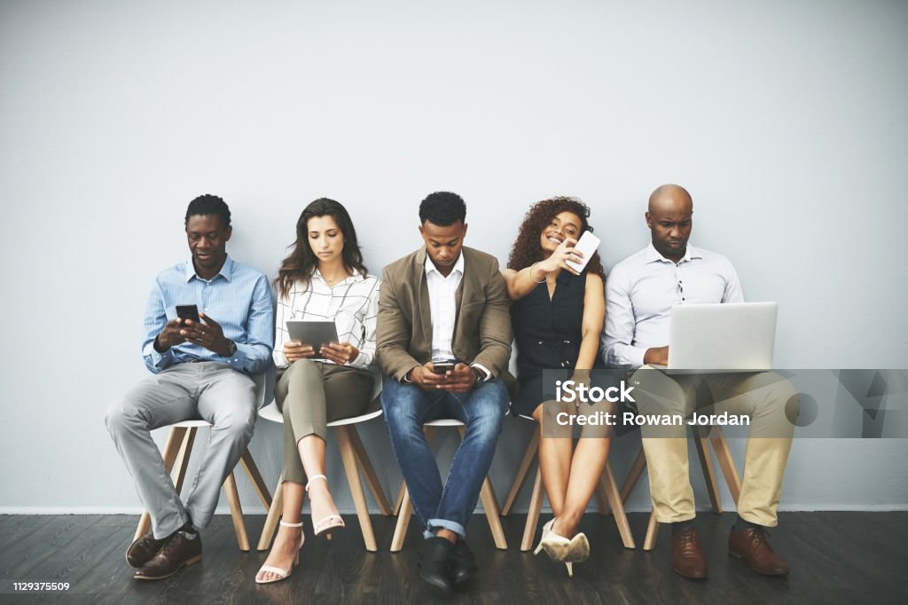 Time to ace the interview but first a selfie Studio shot of a group of businesspeople using their wireless devices while waiting in line Job Interview Stock Photo