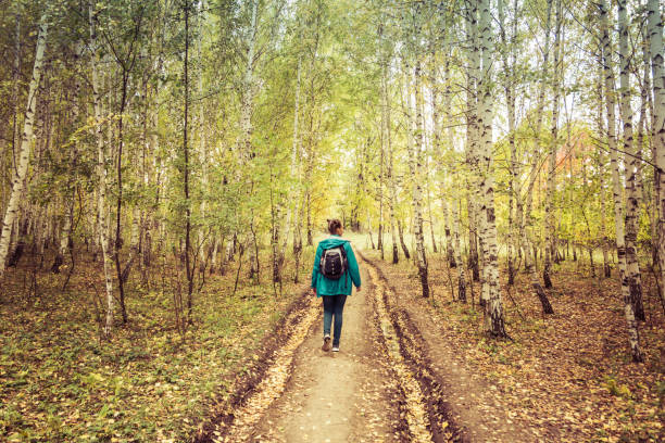 istock Girl with a backpack walks through the autumn forest 1129377082
