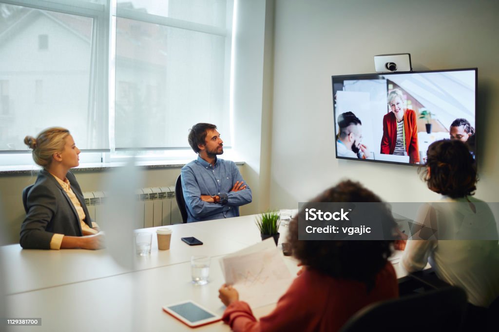 Business People Having a Video Call Business People Having a Video Call in Board Room. Sitting by the desk and talking with coworkers on lcd tv. Meeting Stock Photo