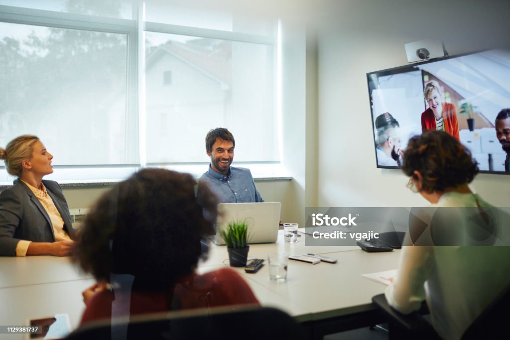 Business People Having a Video Call Business People Having a Video Call in Board Room. Sitting by the desk and talking with coworkers on lcd tv. Meeting Room Stock Photo