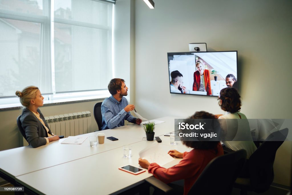 Business People Having a Video Call Business People Having a Video Call in Board Room. Sitting by the desk and talking with coworkers on lcd tv. Meeting Room Stock Photo