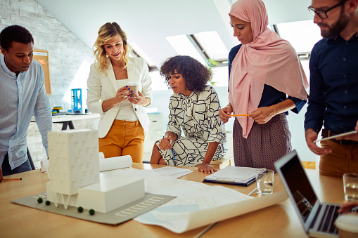 Diverse business team of architects have meeting in the office.Standing i front of blueprints and architectural model and discussing about their new project.