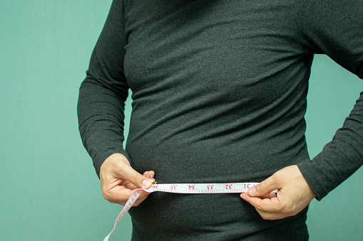 full man with belly measures the volume of his waist