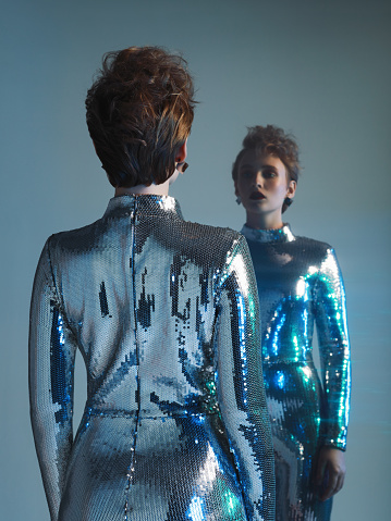 Woman in futuristic sequins jumpsuit and her mirror reflection