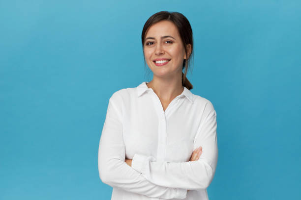 Businesswoman studio portrait. Confidence woman in elegant white shirt isolated on blue Amazing and cheerful smiling brunette with crossed arms in white shirt studio shot, isolated on blue button down shirt stock pictures, royalty-free photos & images