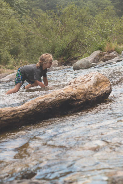 istock A boy with long hair crawsl though a wilderness creek 1129389866