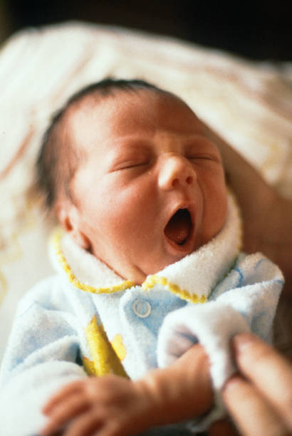 A vertical image of a newborn infant yawning. The image shows the baby's head with black hair and part of his shoulders. Image conjures up thoughts such a young, innocence, family, togetherness, tenderness, and love