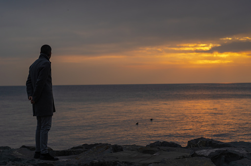 Young man is standing on a ledge of a sea, enjoying the beautiful sunset over a sea in Istanbul,Turkey.