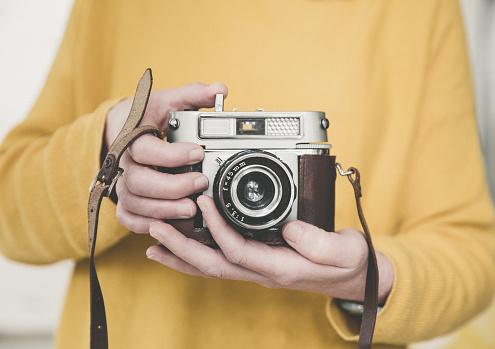 A midsection of a girl holiding a vintage, 35mm camera in yellow with copy space
