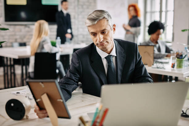 istock Pensive businessman looking at photo in picture frame at work. 1129400277