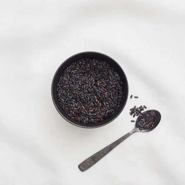 Black Rice in a small bowl with a spoon on a white linen table cloth