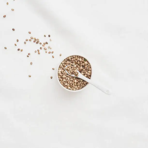 Hemp Seeds in a small bowl with a small spoon on a white linen table cloth