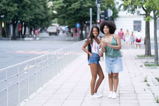 istock Two girlfriends having fun on street and using phone 1129415711
