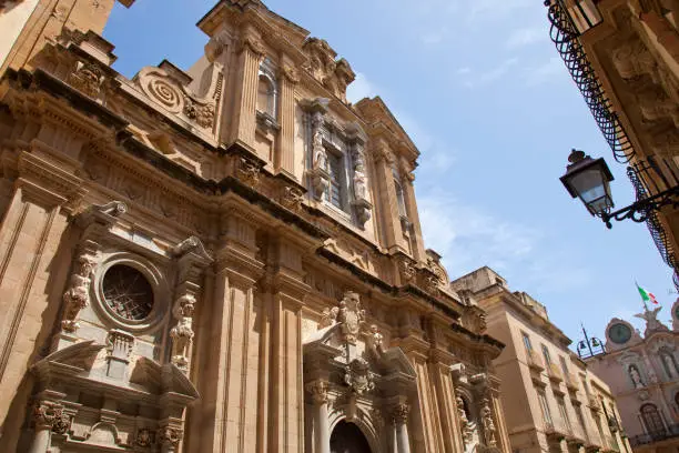 Photo of Trapani Sicily Scene showing the facade of the Church of the Jesuit College in the historic center of Trapani and the Cavarretta Palace at the end of the street.