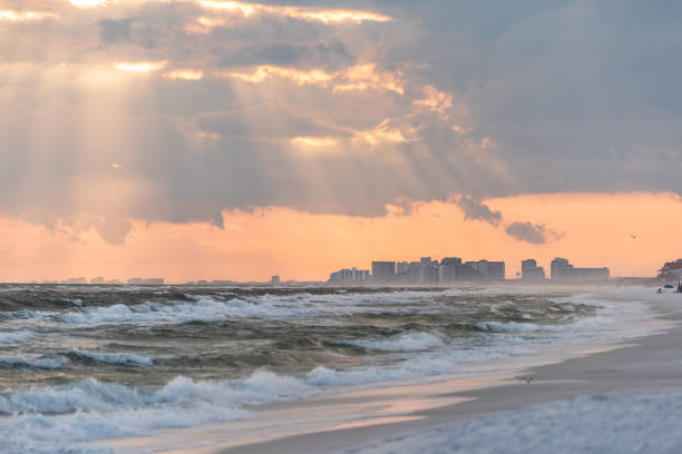 dramatic magical pastel light sunset with sun rays in santa rosa beach, florida with pensacola coastline coast cityscape skyline in panhandle and ocean gulf mexico waves - florida weather urban scene dramatic sky imagens e fotografias de stock