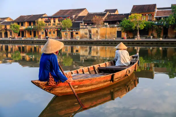 Vietnamese women paddling in old town in Hoi An city, Vietnam. Hoi An is situated on the east coast of Vietnam. Its old town is a UNESCO World Heritage Site because of its historical buildings.