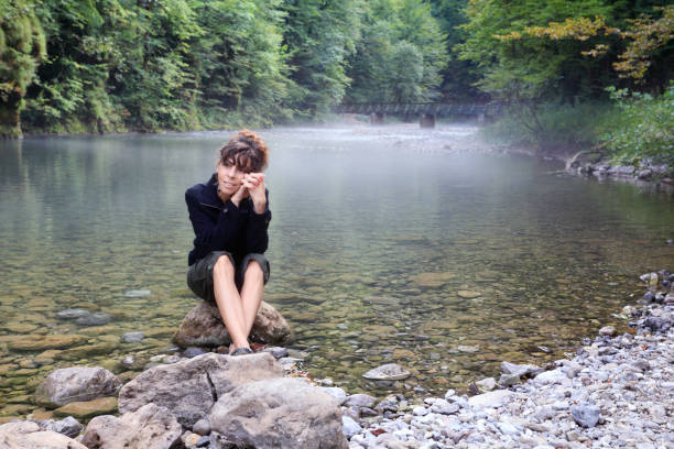 The woman alone covered her head with her hands and cries in the open air. Stormy river, mountains on the background.
