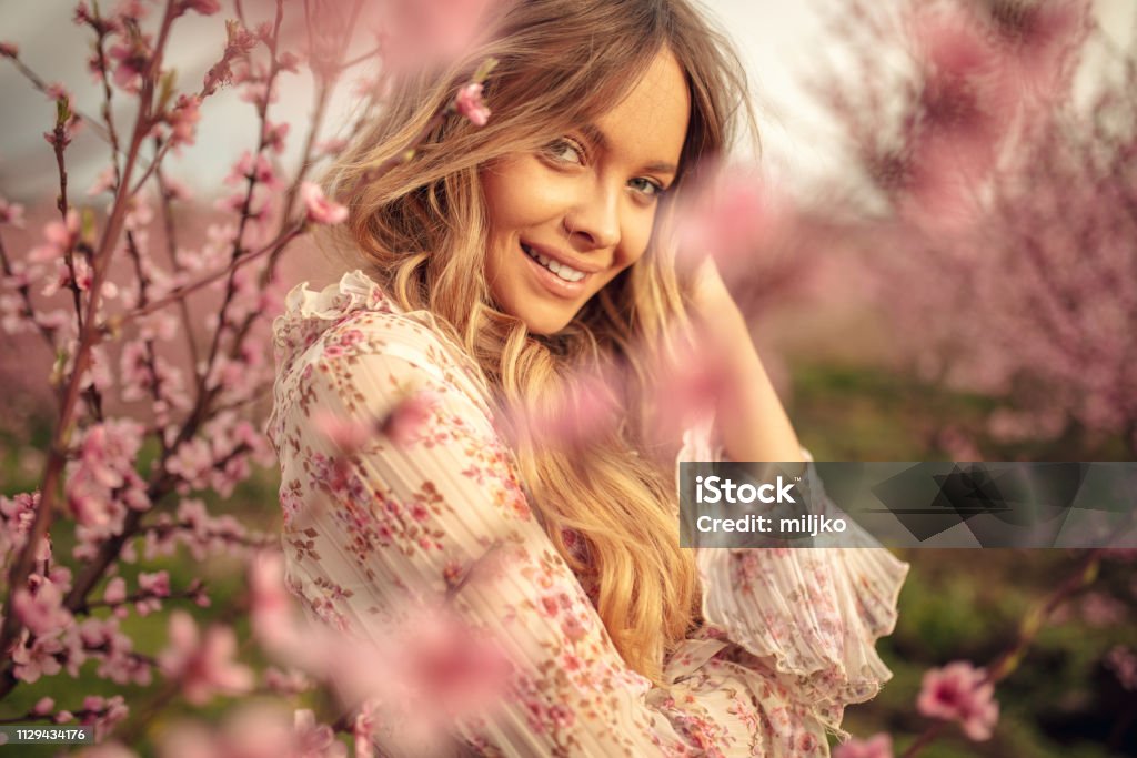 Amazing young woman posing in apricot tree orchard at spring Portrait of amazing and beautiful young woman at spring in orchard of apricot trees in blossom. She is cheerful and happy, enjoying springtime. Women Stock Photo