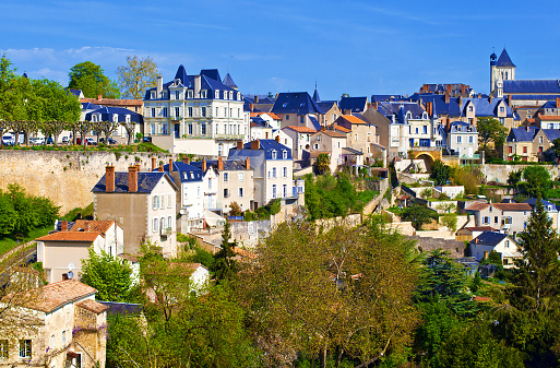 View on a small town of Thouars, France. Many houses with towers and gray roofs among green trees and rooftops. Warm spring morning, vibrant blue sky with clouds, calm atmosphere, skyline