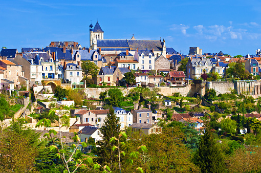 View on a small town of Thouars, France. Many houses with towers and gray roofs among green trees and rooftops. Warm spring morning, vibrant blue sky with clouds, calm atmosphere, skyline