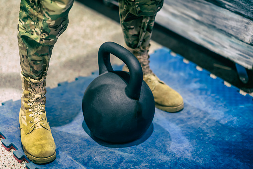 Legs of abstract athlete in camouflage pants and in yellow boots near kettlebell closeup, preparation before heavy lifting weight