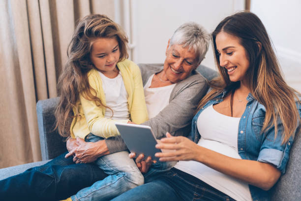 trois femmes de génération sont amuser à la maison - wireless technology cheerful granddaughter grandmother photos et images de collection