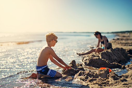 Brother and sister playing soccer on beach. The boy aged 8 is holding the ball and laughing at the camera.\nNikon D850