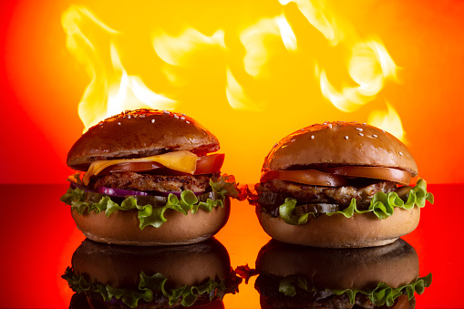 two homemade hamburgers with beef and cucumbers on fire background Copy space