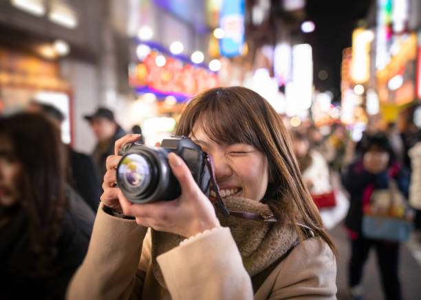 istock Young woman taking pictures using digital camera on crowded street at night 1129468520
