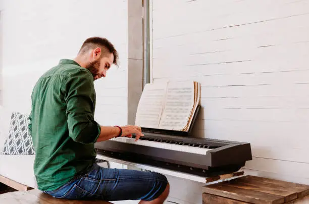 Photo of Young man playing electric piano at home studio