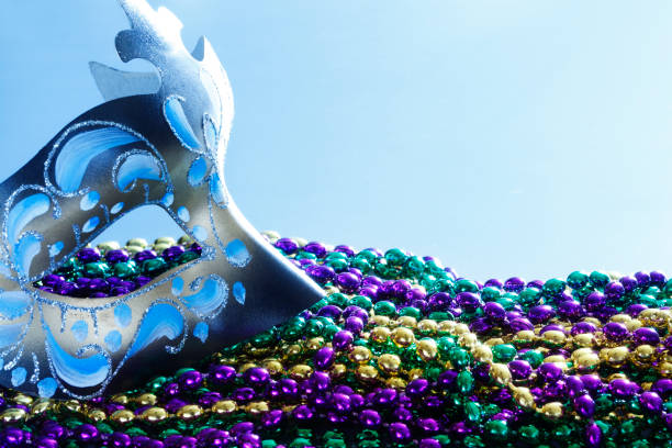 Mardi Gras Mask And Beads A Mardi Gras mask and a pile of colorful beads in front of light blue background. purple and gold masquerade masks stock pictures, royalty-free photos & images
