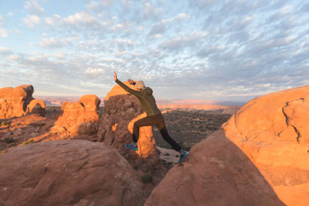 istock Female hiker leaping across a boulder in the Utah desert 1129486546