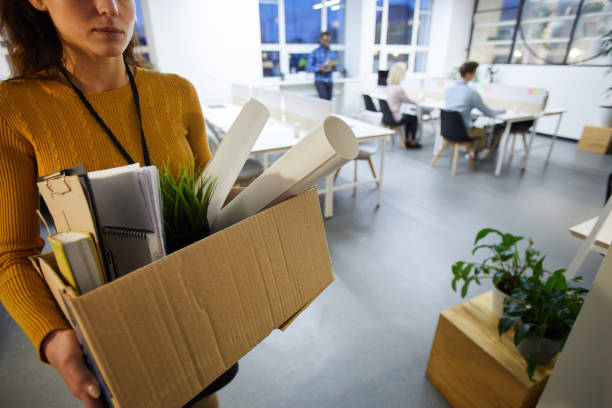 Leaving office after dismissal Serious sad woman in sweater carrying cardboard box full of stuff and leaving office after dismissal resignation stock pictures, royalty-free photos & images