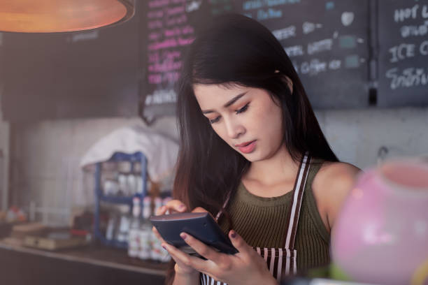 istock Young asian cashier woman using tablet at cafe background, work concept. 1129534946