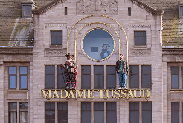 Amsterdam, Netherlands - MAY 17, 2018: Famous Madame Tussaud wax museum exterior entrance in Amsterdam with gold logo and figurines from exhibition on top of it and circle window with people inside looking at waxworks.
