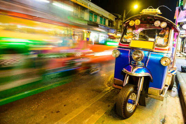 blurred traffic passing a parked tuk tuk taxi, bangkok, thailand - jinrikisha thailand tuk transportation imagens e fotografias de stock