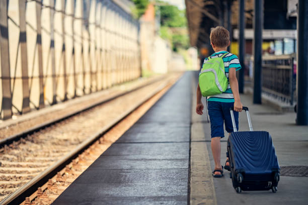 Little boy walking on train station. The kid is pulling his suitcase on his way to summer camp.\nNikon D850