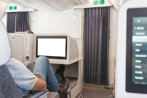 Luxury business class seat in a modern airplane with wide monitor displaying a blank white background for your design.