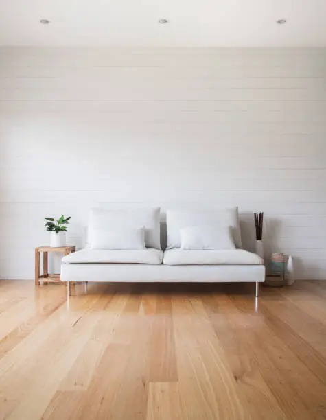 Stylish living room scene with white VJ panelling walls, white couch and timber floor. Lots of copy space.