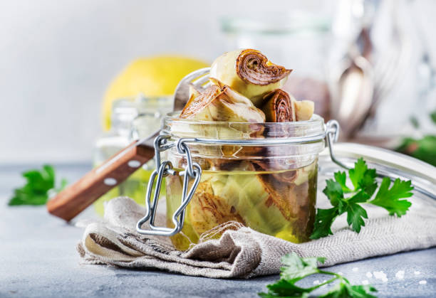 Canned artichokes in olive oil, in glass jar with fork, gray kitchen table, selective focus