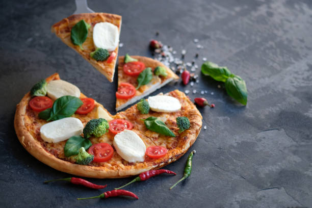 istock Sliced pizza with Mozzarella cheese, tomatoes, broccoli, Spices and fresh basil. Italian pizza. Pizza on black stone background 1129565604
